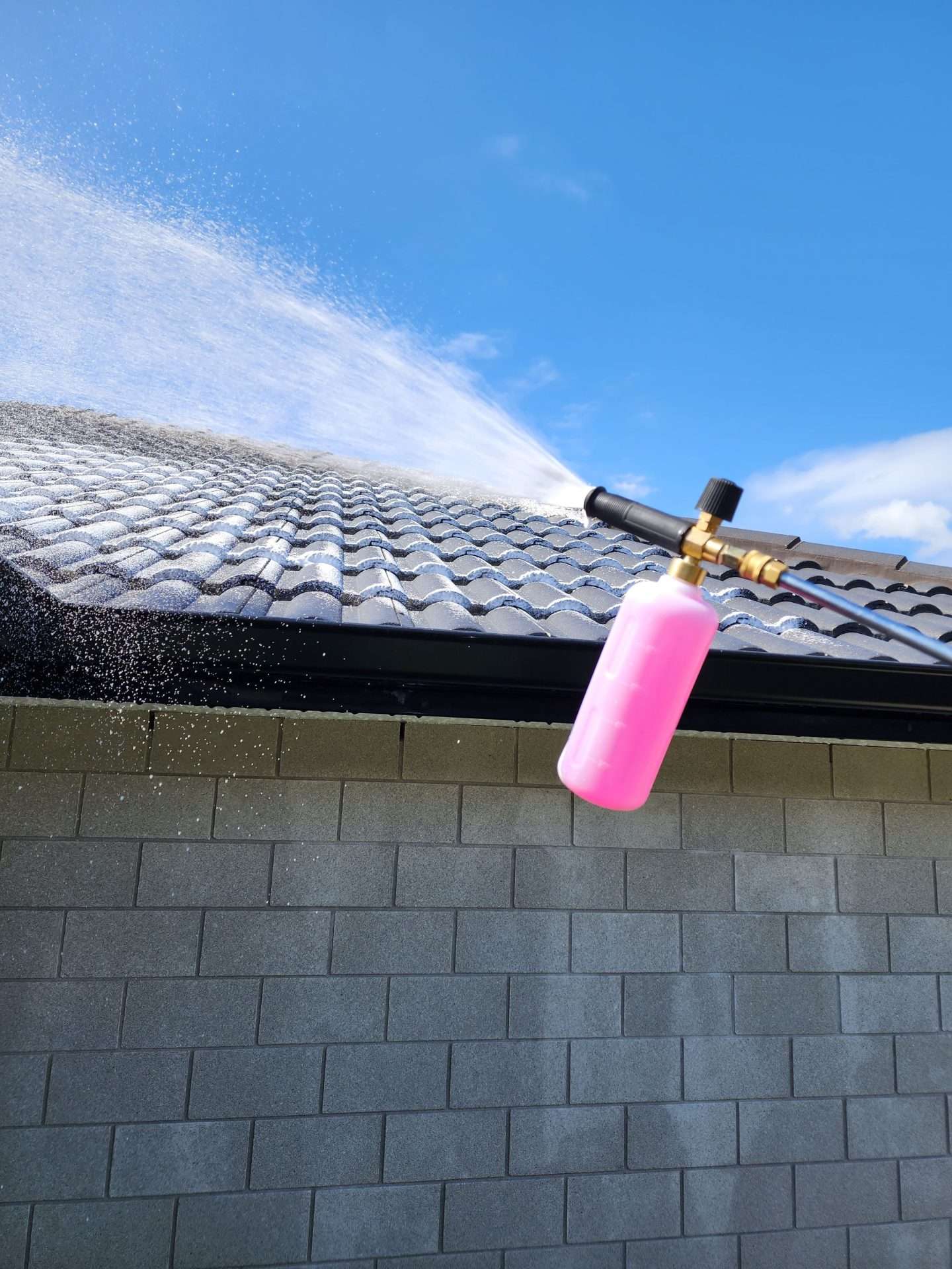 a hose with a detergent attached spraying the roof of a house to wash it